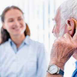 Older patient wearing a hearing aid while talking to his audiologist.