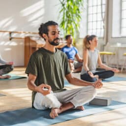 Group yoga class in the middle of meditation. Close up on a young man in a green shirt on a yoga mat in butterfly pose.