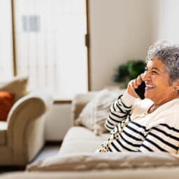 Smiling woman in her living room on a phone call, scheduling a hearing appointment.