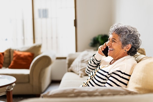 Smiling woman in her living room on a phone call, scheduling a hearing appointment.
