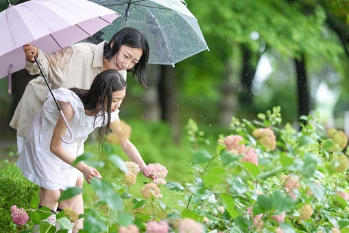 Mother and daughter holding umbrellas on a humid rainy spring day smelling the flowers.