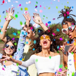Group of happy beautiful young friends throwing confetti at an outdoor music festival.