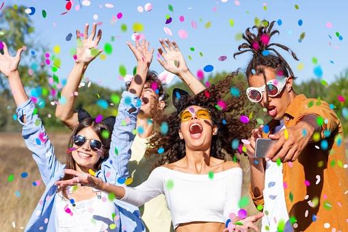 Group of happy beautiful young friends throwing confetti at an outdoor music festival.