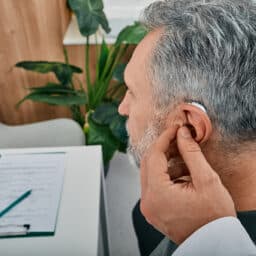 Patient at an audiologist clinic gets a new hearing aid fitted by a doctor, off-camera.