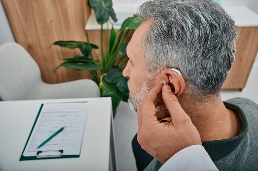 Patient at an audiologist clinic gets a new hearing aid fitted by a doctor, off-camera.