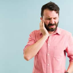Worried man in his 30s aching and listening to a ringing in his ear. Pained man with touching his ears because of tinnitus