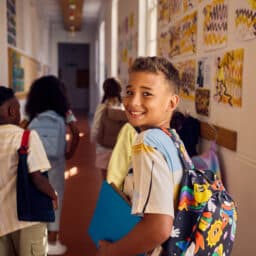 choolboy carrying book and backpack walking in school corridor with classmates