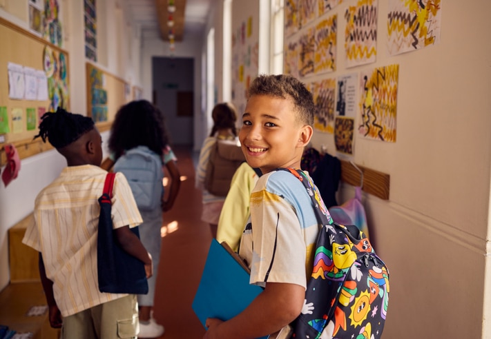choolboy carrying book and backpack walking in school corridor with classmates