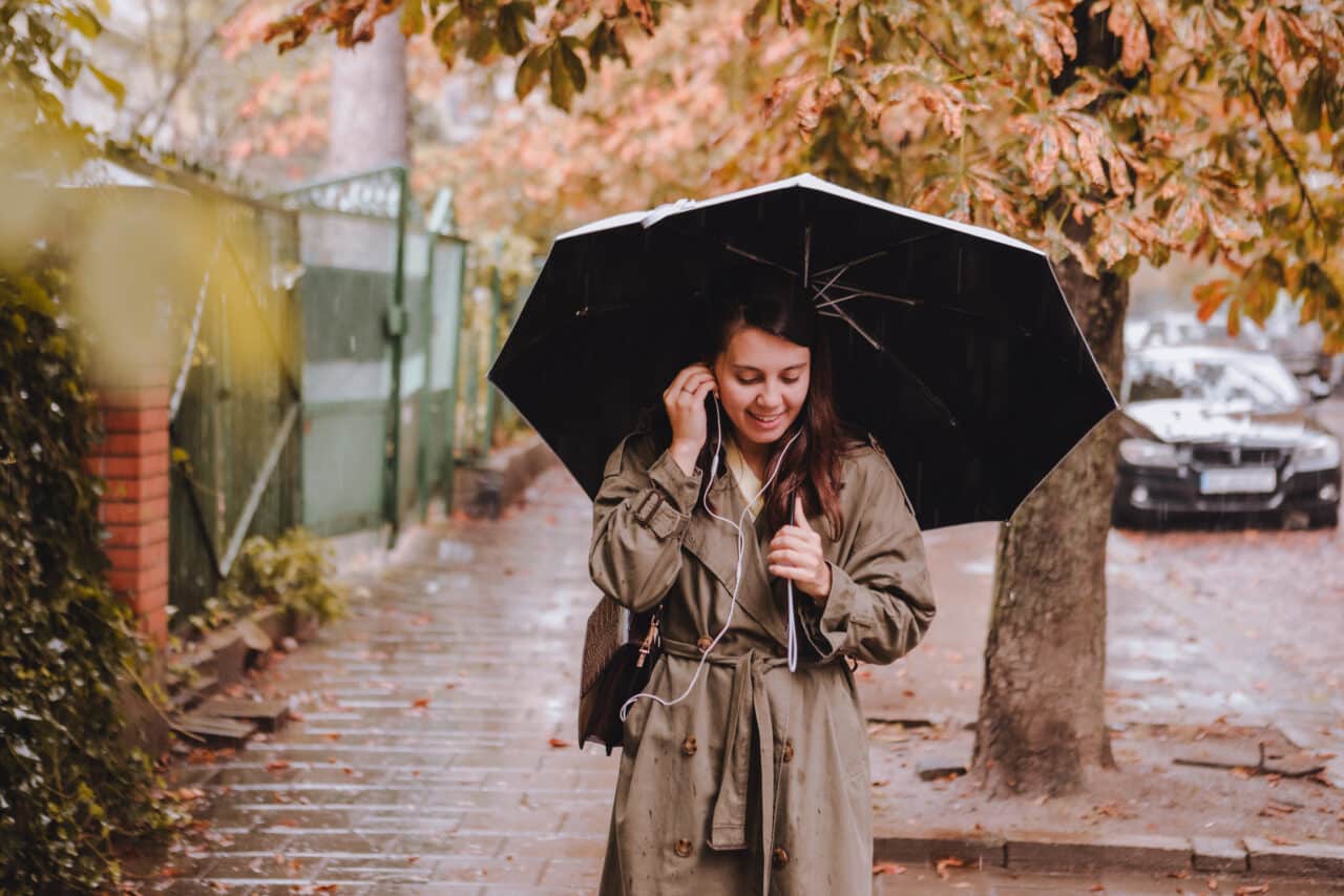 Woman wearing a stylish coat and holding an umbrella walking down the street in the rain on a beautiful fall day.