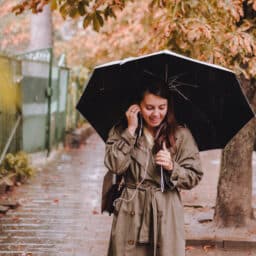 Woman wearing a stylish coat and holding an umbrella walking down the street in the rain on a beautiful fall day.